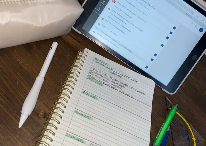 Ein Tablet liegt auf einem Tisch, darunter ein Notizblock. Daneben befinden sich ein weißes Mäppchen, ein Digitalstift, mehrere Stifte und ein Geodreieck.