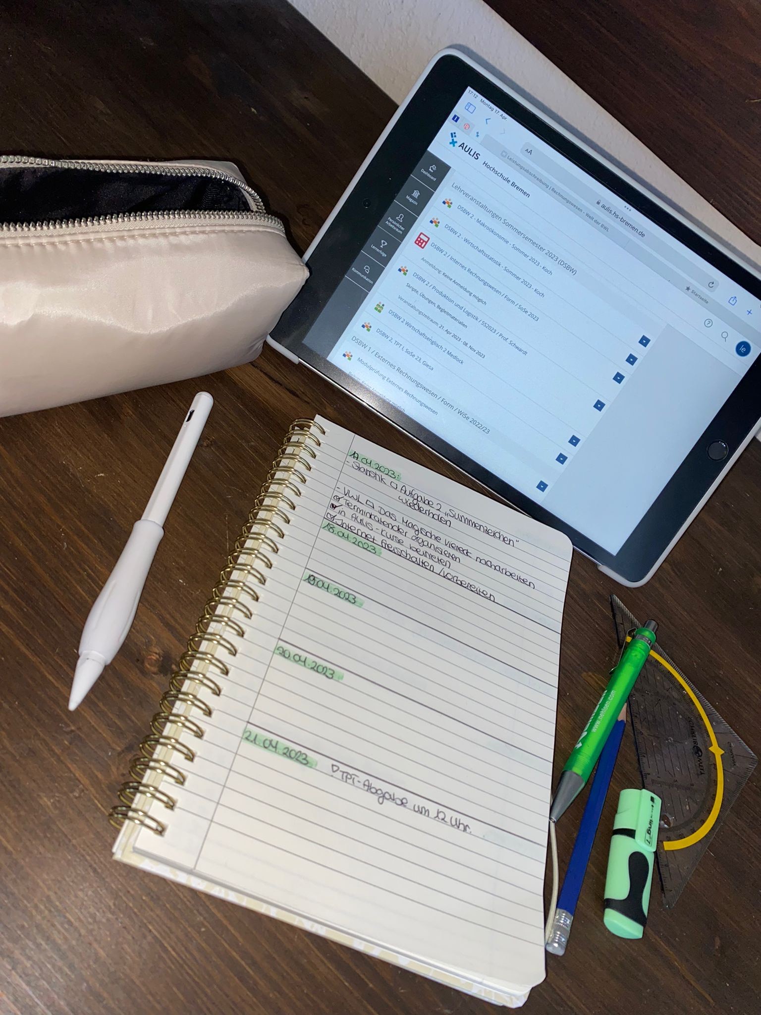 Ein Tablet liegt auf einem Tisch, darunter ein Notizblock. Daneben befinden sich ein weißes Mäppchen, ein Digitalstift, mehrere Stifte und ein Geodreieck.