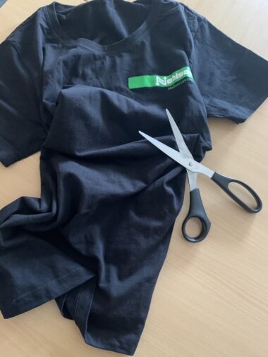 Ein dunkelblaues T-Shirt liegt auf einem Tisch. Darauf liegt eine Schere.