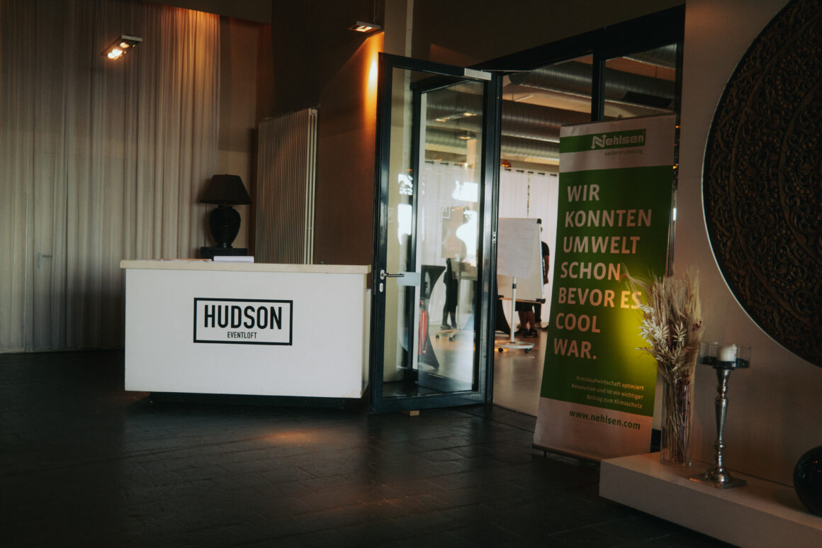 Empfangsraum einer Gaststätte. Links von der Tür steht ein Empfangstresen mit der Aufschrift Hudson.